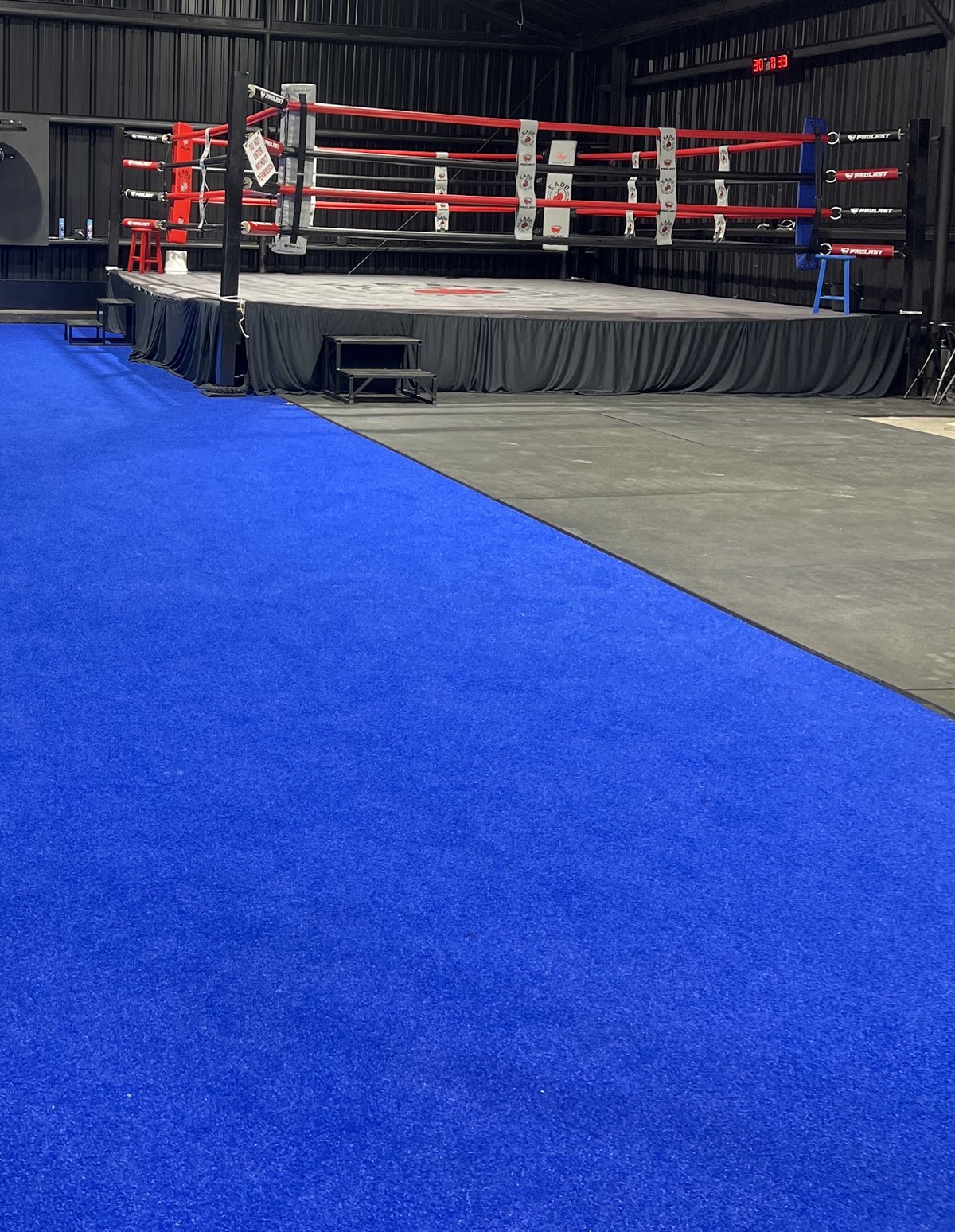 The boxing ring with blue ropes set on blue turf inside the warehouse